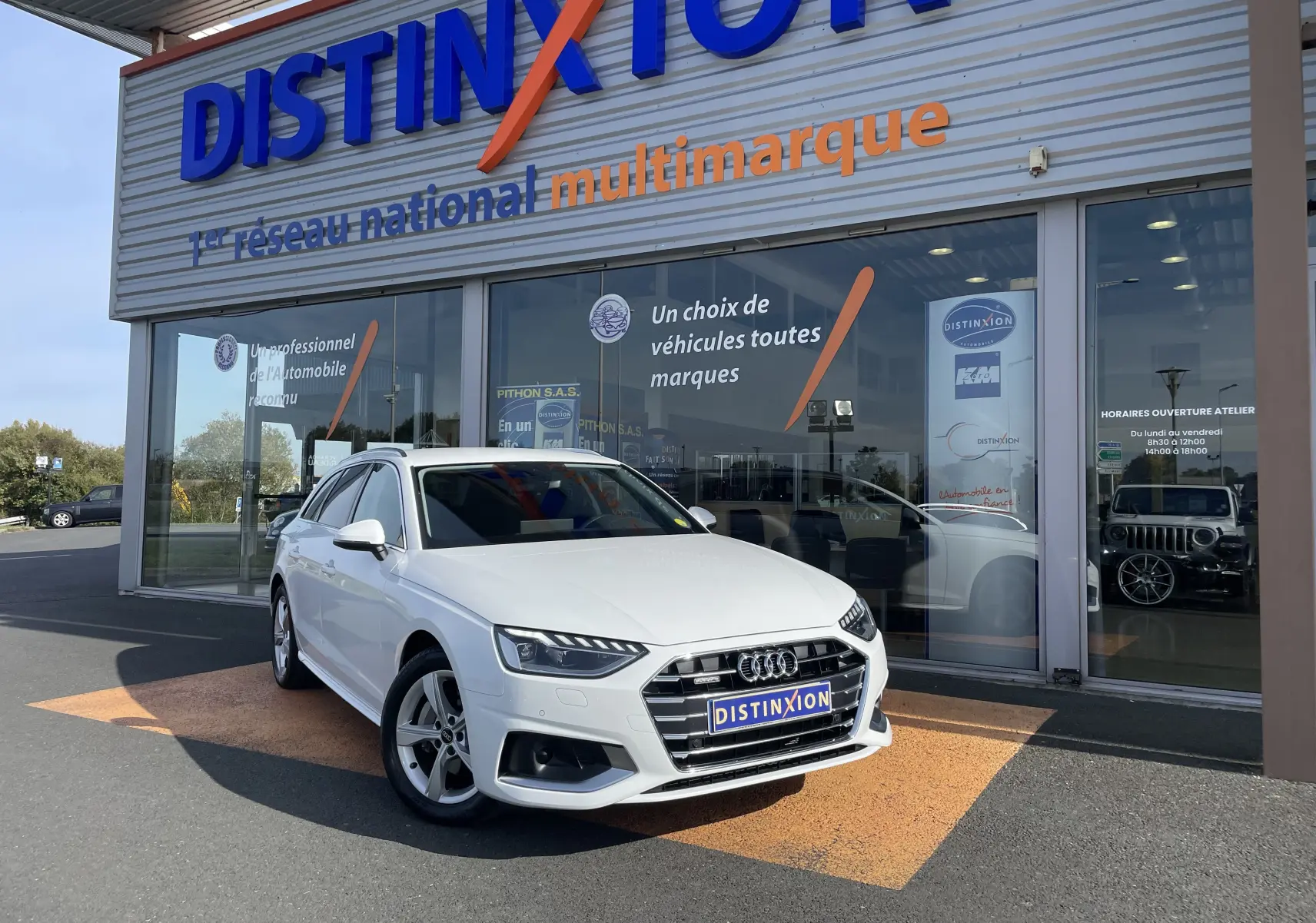 Audi A4 Avant blanc vue 3/4 avant droit, stationnée devant un showroom Distinxion avec logo visible.