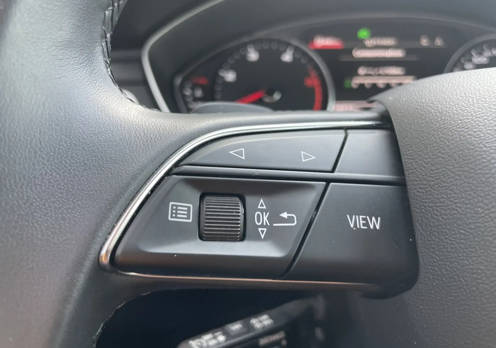 Gros plan sur les commandes gauche au volant d'une Audi A4 Avant 40 TDI 2022, avec tableau de bord flou en arrière-plan.