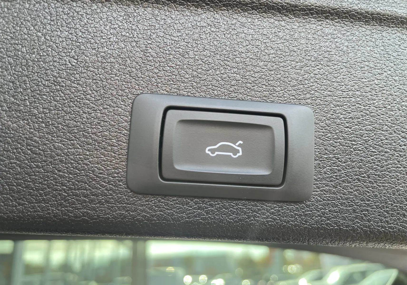 Bouton noir de déverrouillage du hayon sur fond de garniture intérieure texturée d'une Audi A4 Avant blanche 2022.