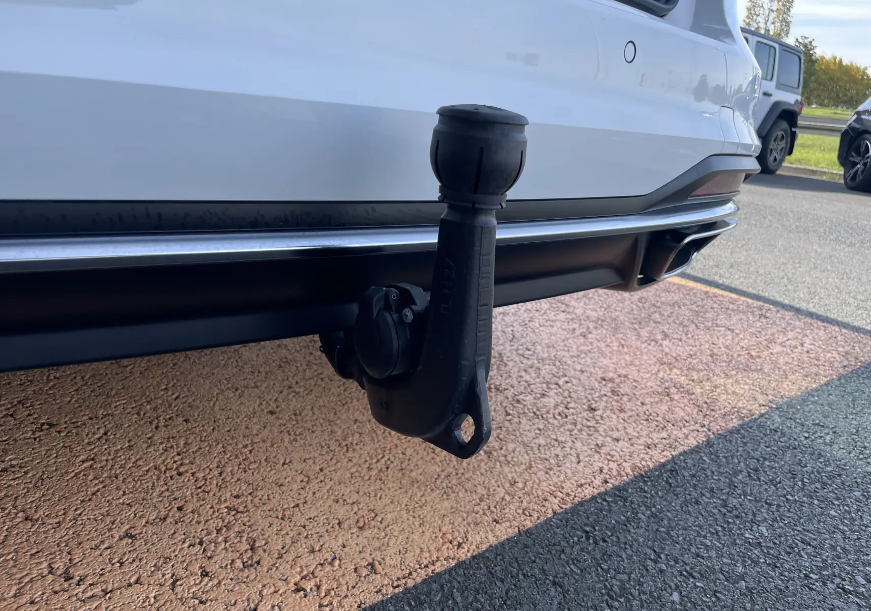 Gros plan sur l'attelage arrière noir d'une Audi A4 Avant 40 TDI blanche, vue côté droit en extérieur.