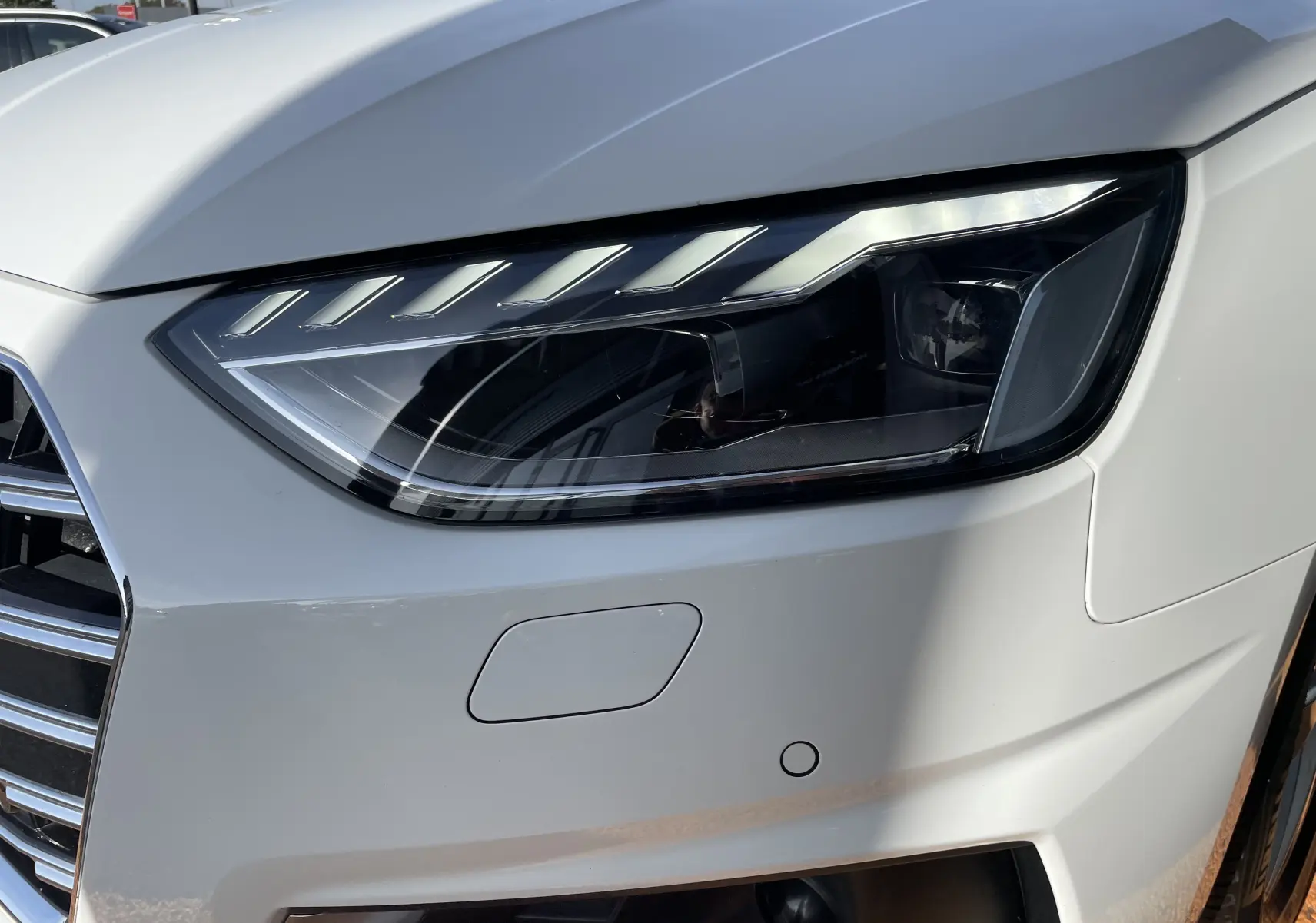 Gros plan sur le phare avant droit blanc d'une Audi A4 Avant 40 TDI 2022 avec calandre chromée et capteur de stationnement.