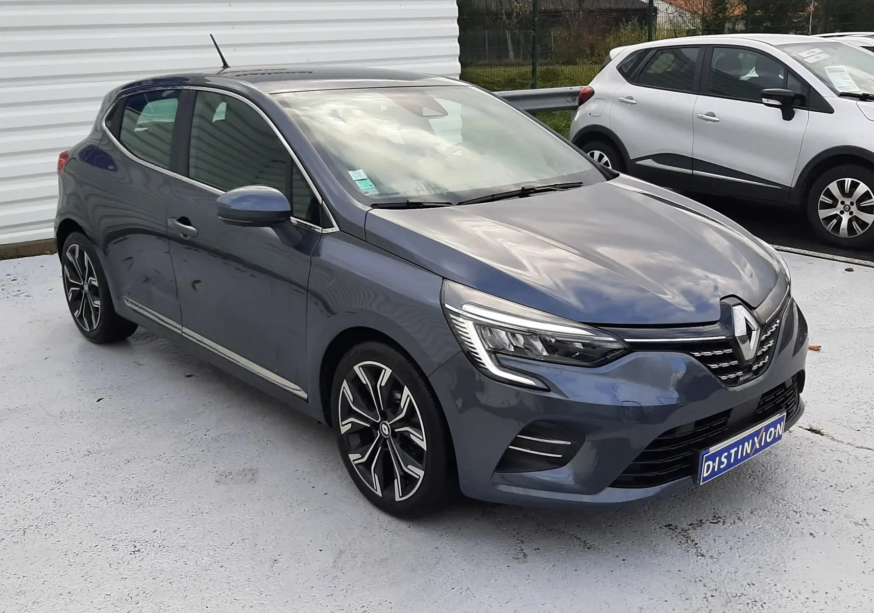 Renault Clio V TCE 90 Intens gris titanium vue 3/4 avant droit, avec jantes alliage et feux LED allumés.
