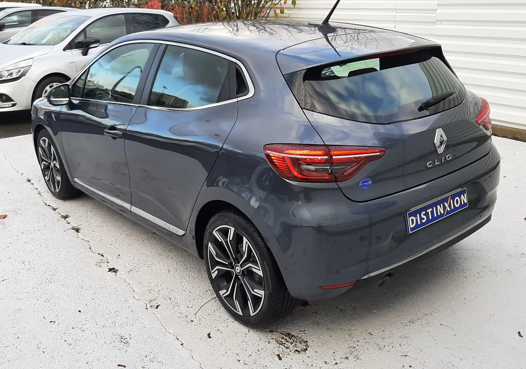 Renault Clio V gris titanium vue 3/4 arrière droit, avec jantes alliage noires et feux arrière LED distinctifs.