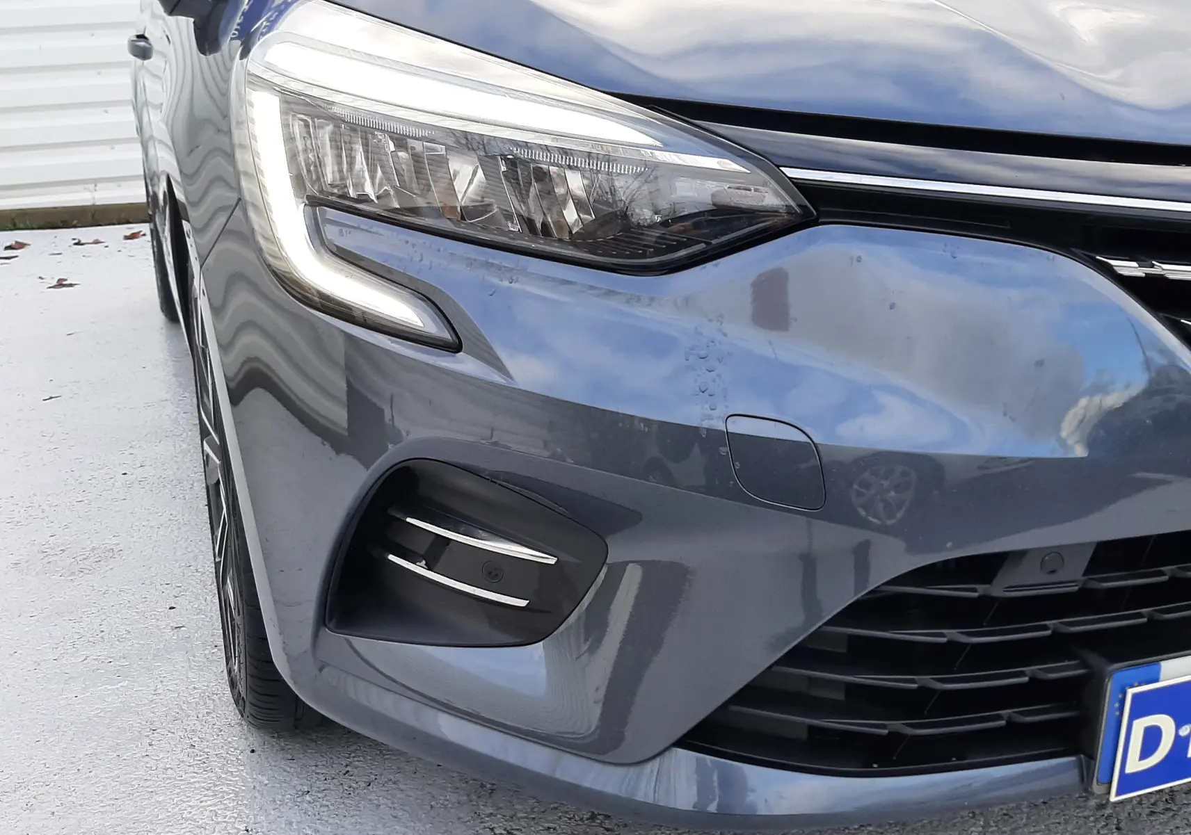 Gros plan sur le phare avant gauche et la calandre d'une Renault Clio V gris titanium, version TCE 90 Intens X-Tronic.