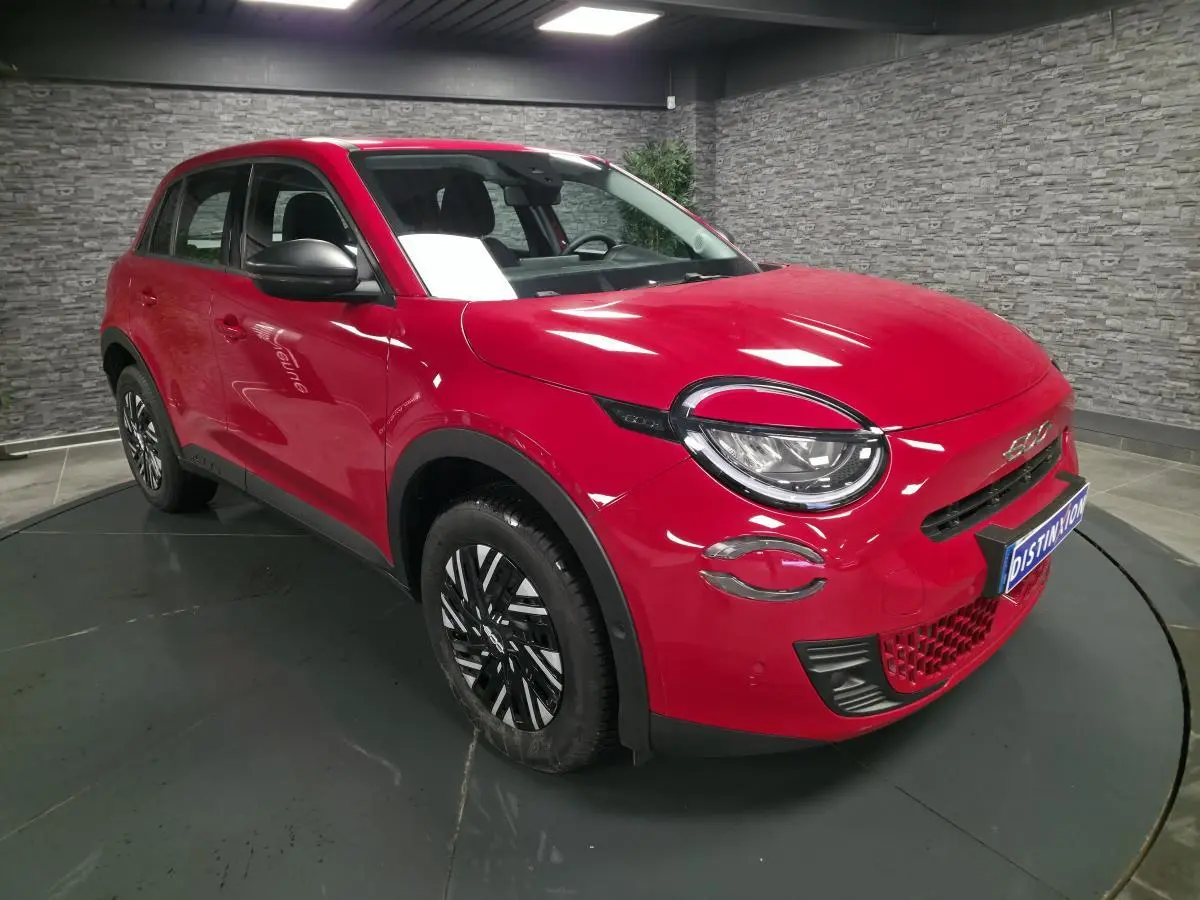 Vue 3/4 avant droite d'une FIAT 600 rouge avec phares LED et jantes bicolores en intérieur showroom.