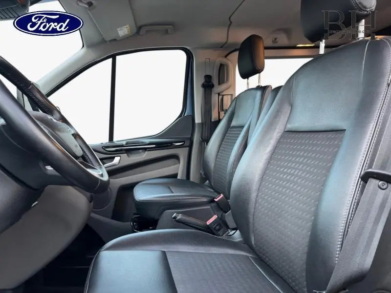 Vue intérieure côté gauche du Ford Transit Custom Fourgon 2023, sièges avant en cuir noir avec volant cuir visible.