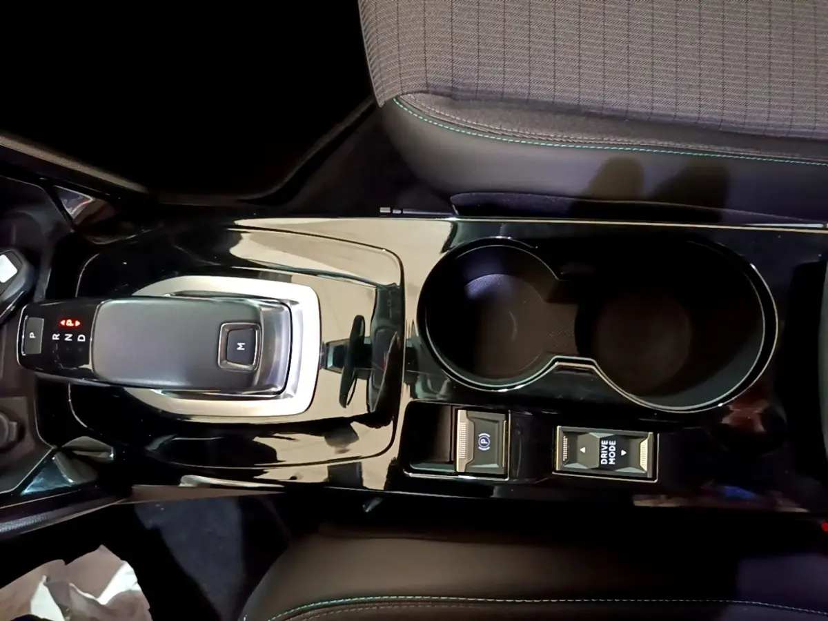 Vue plongeante sur la console centrale noire brillante du Peugeot 2008 orange, avec levier de vitesse automatique et porte-gobelets.
