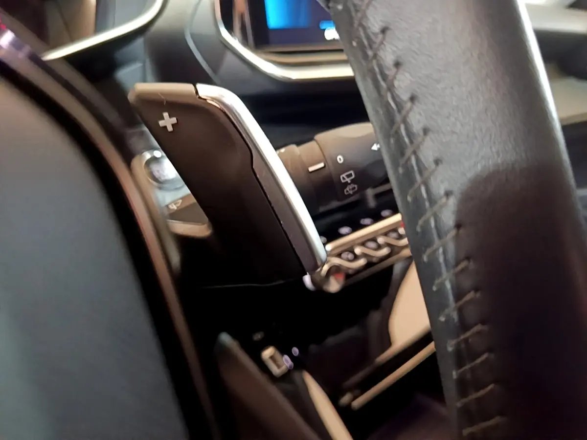 Gros plan sur la palette de changement de vitesse droite en cuir noir, volant et tableau de bord numérique du Peugeot 2008.