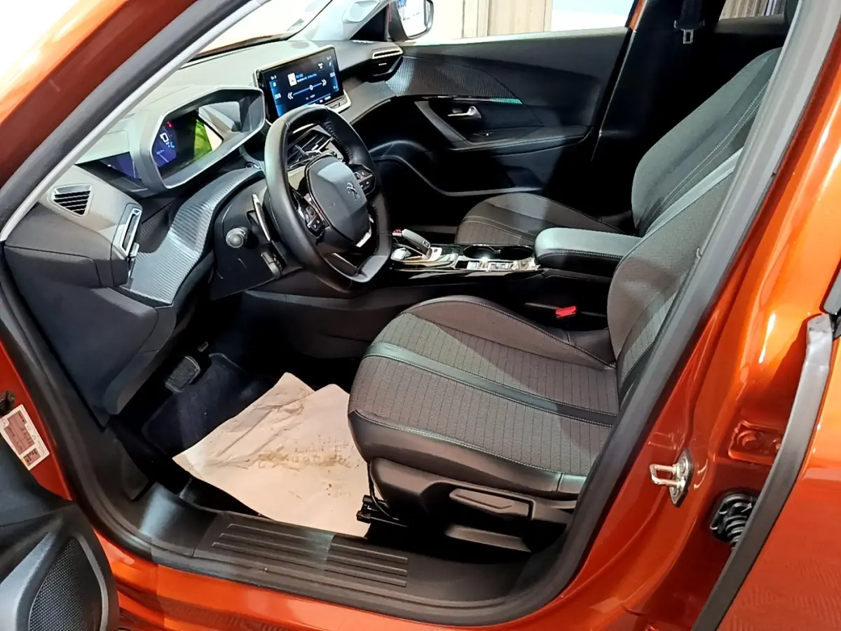 Intérieur de la Peugeot 2008 orange vue côté conducteur, montrant sièges tissu, volant cuir et tableau de bord digital.