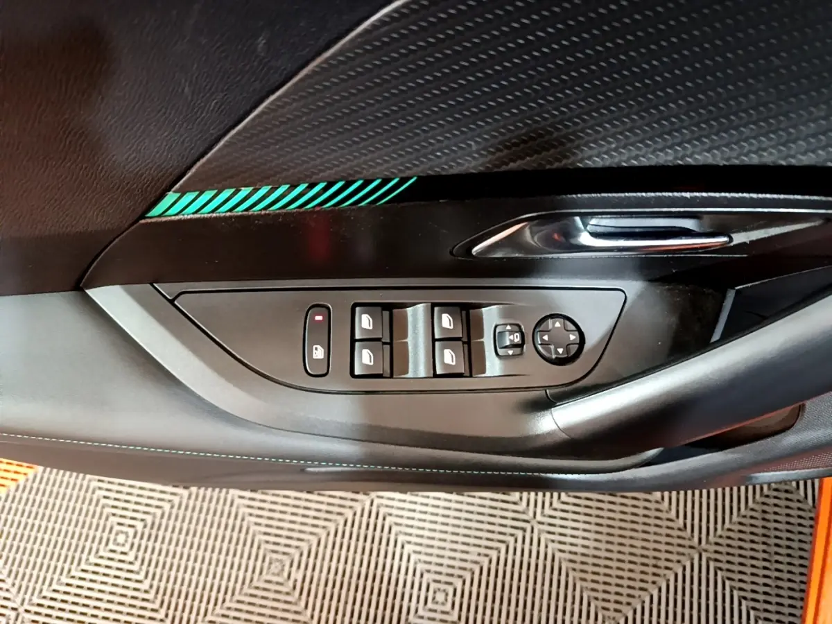 Détail de la porte côté gauche de la Peugeot 2008 orange, avec commandes des vitres et poignée chromée.