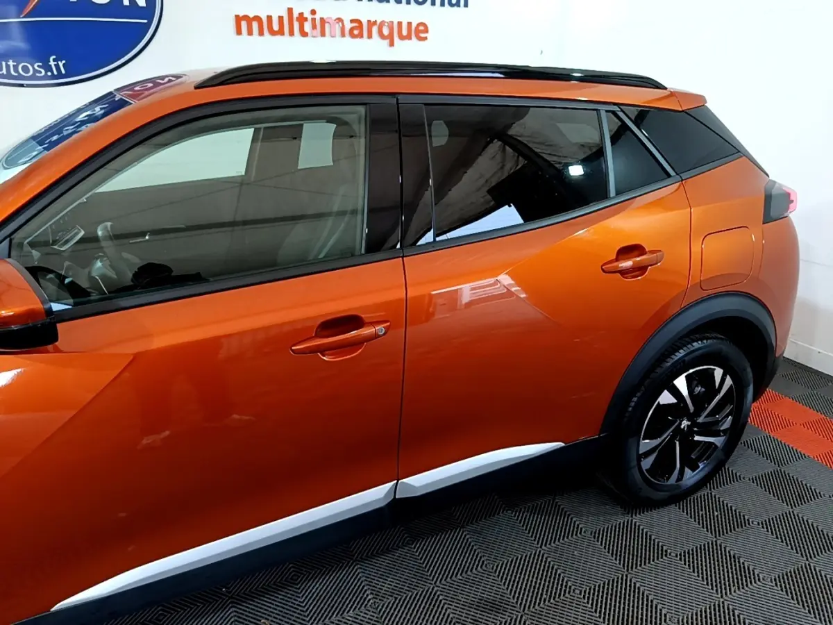 Vue de profil côté gauche du Peugeot 2008 orange 2021 avec jantes noires et toit noir contrasté.