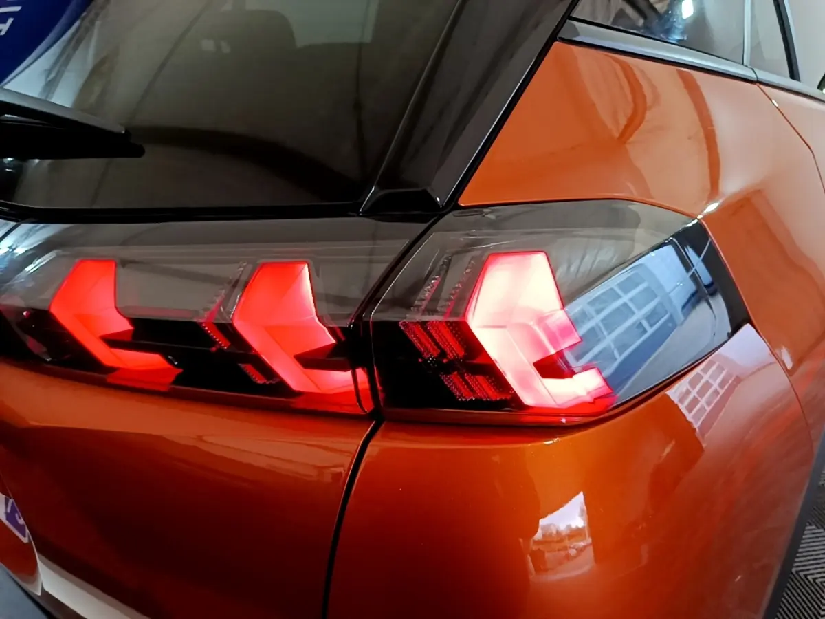 Feu arrière droit allumé d’un Peugeot 2008 orange, vue rapprochée sur la carrosserie et le vitrage noir.
