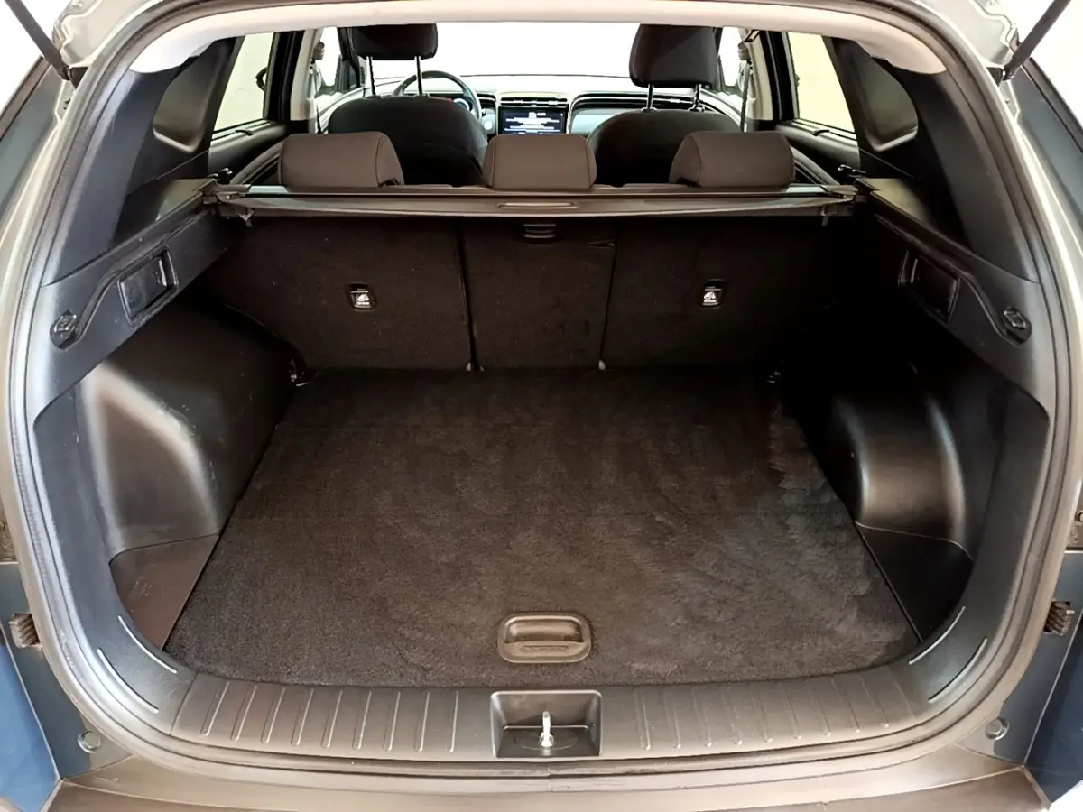 Vue arrière du coffre ouvert du Hyundai Tucson bleu 2023, montrant l'espace de chargement et la tablette cache-bagages.