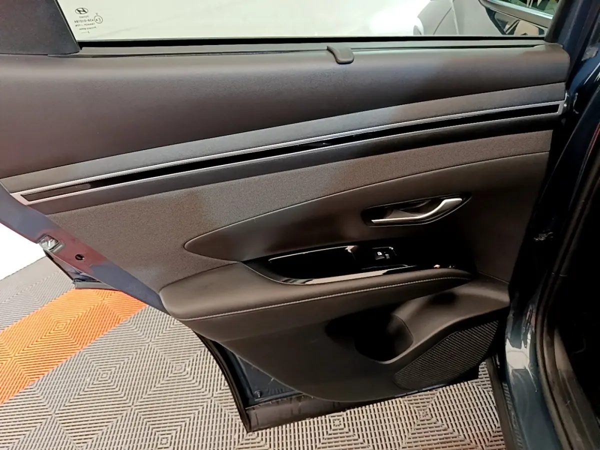 Vue rapprochée de la porte arrière gauche bleu foncé du Hyundai Tucson 2023 avec garniture noire et commande de fenêtre.