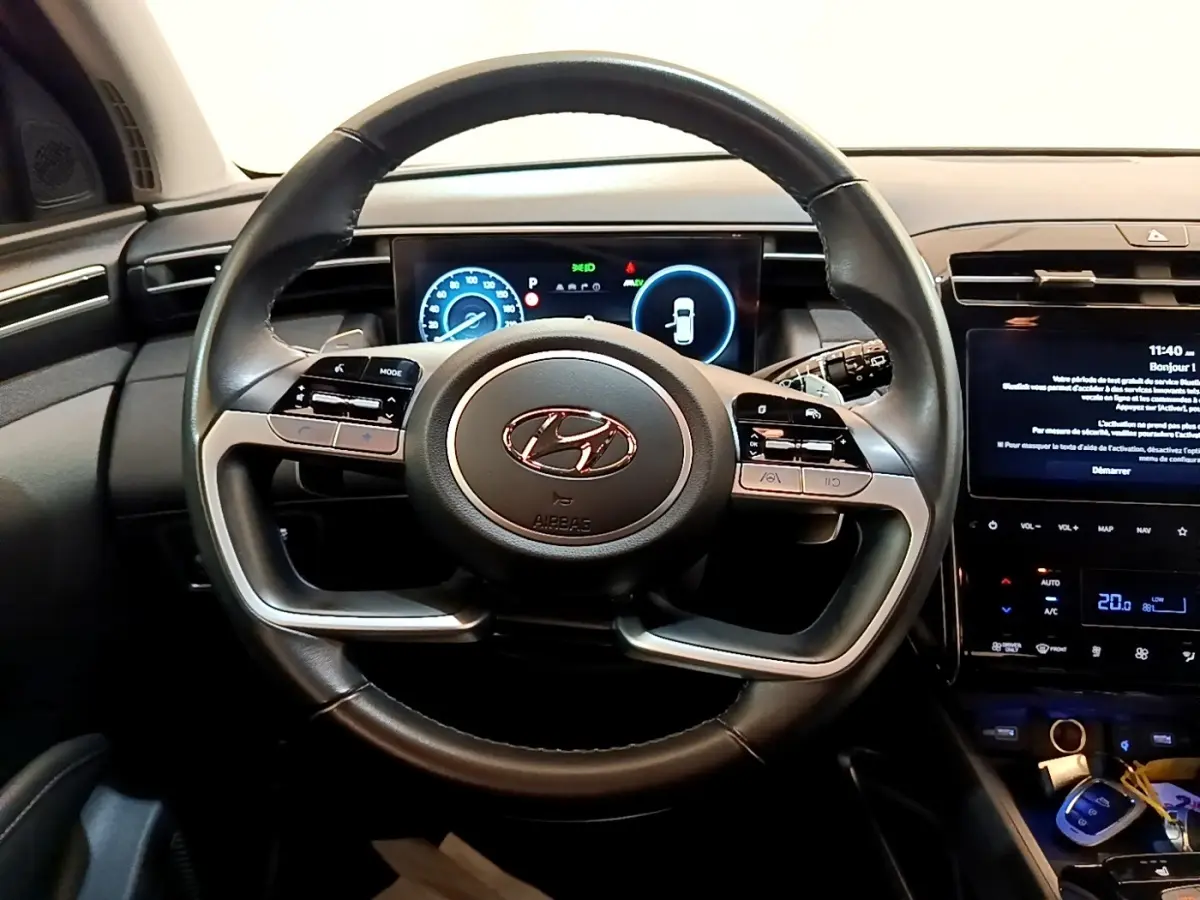 Vue intérieure centrée sur le volant cuir du Hyundai Tucson 2023 avec tableau de bord numérique et écran tactile central.