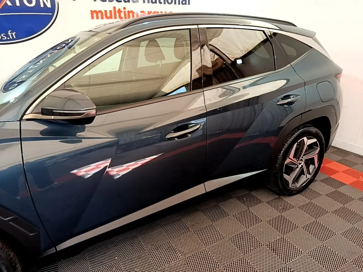Vue latérale côté gauche d’un Hyundai Tucson bleu 2023 avec jantes au design moderne et rétroviseur noir brillant.
