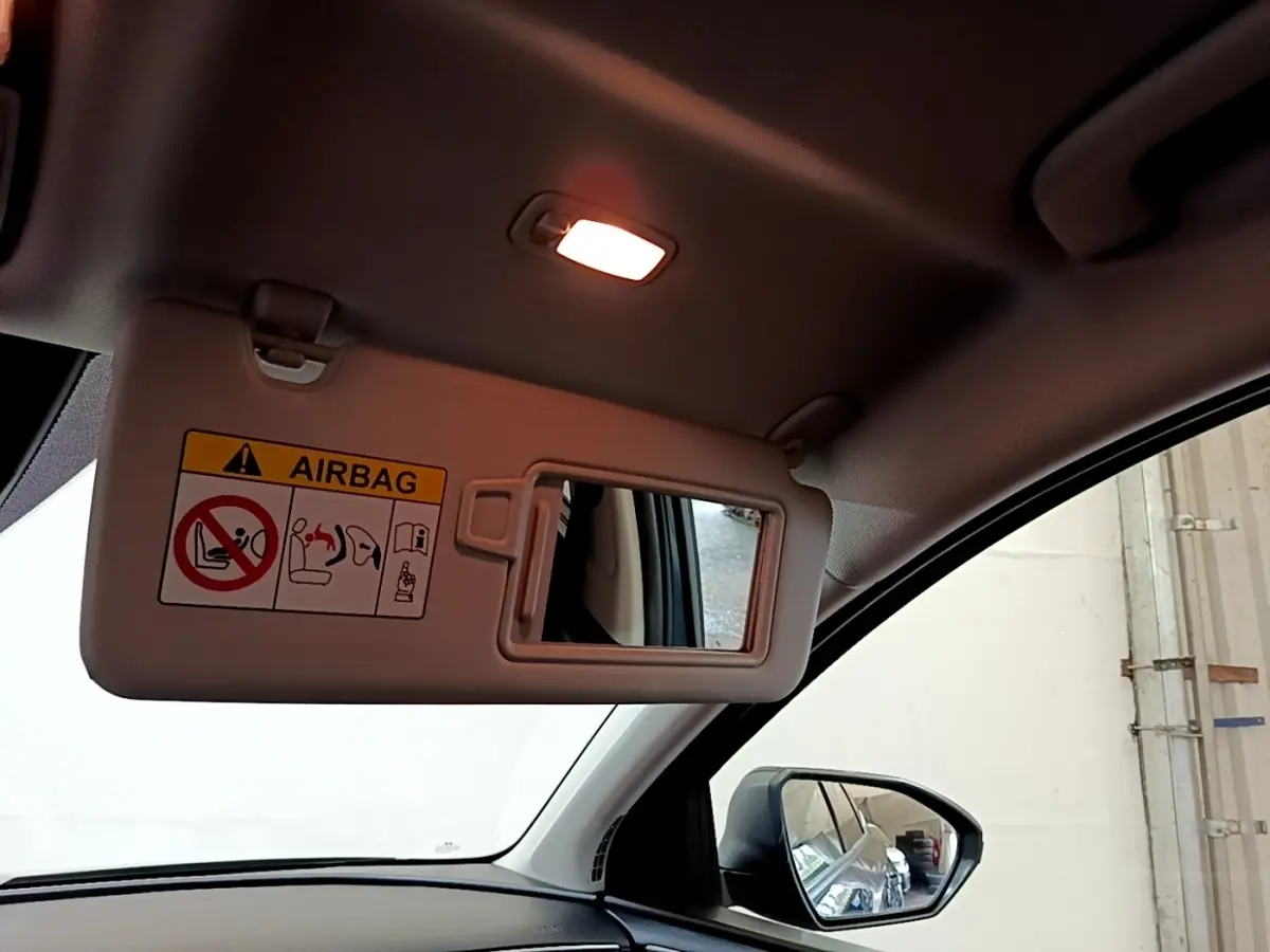 Vue intérieure côté conducteur du pare-soleil avec miroir et avertissement airbag, rétroviseur extérieur visible.