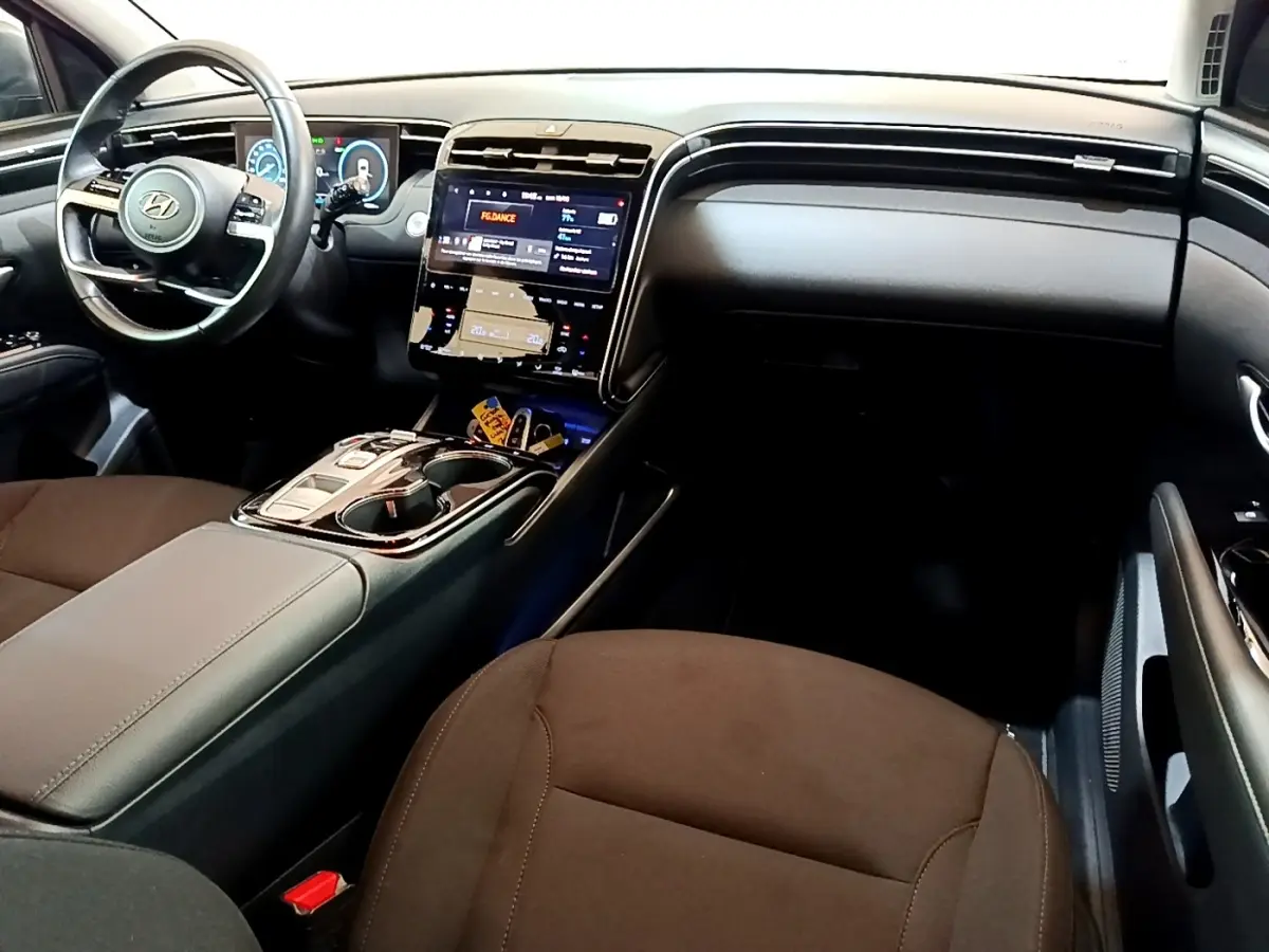 Vue intérieure côté conducteur du Hyundai Tucson 2023, tableau de bord noir avec écran tactile central et volant cuir.