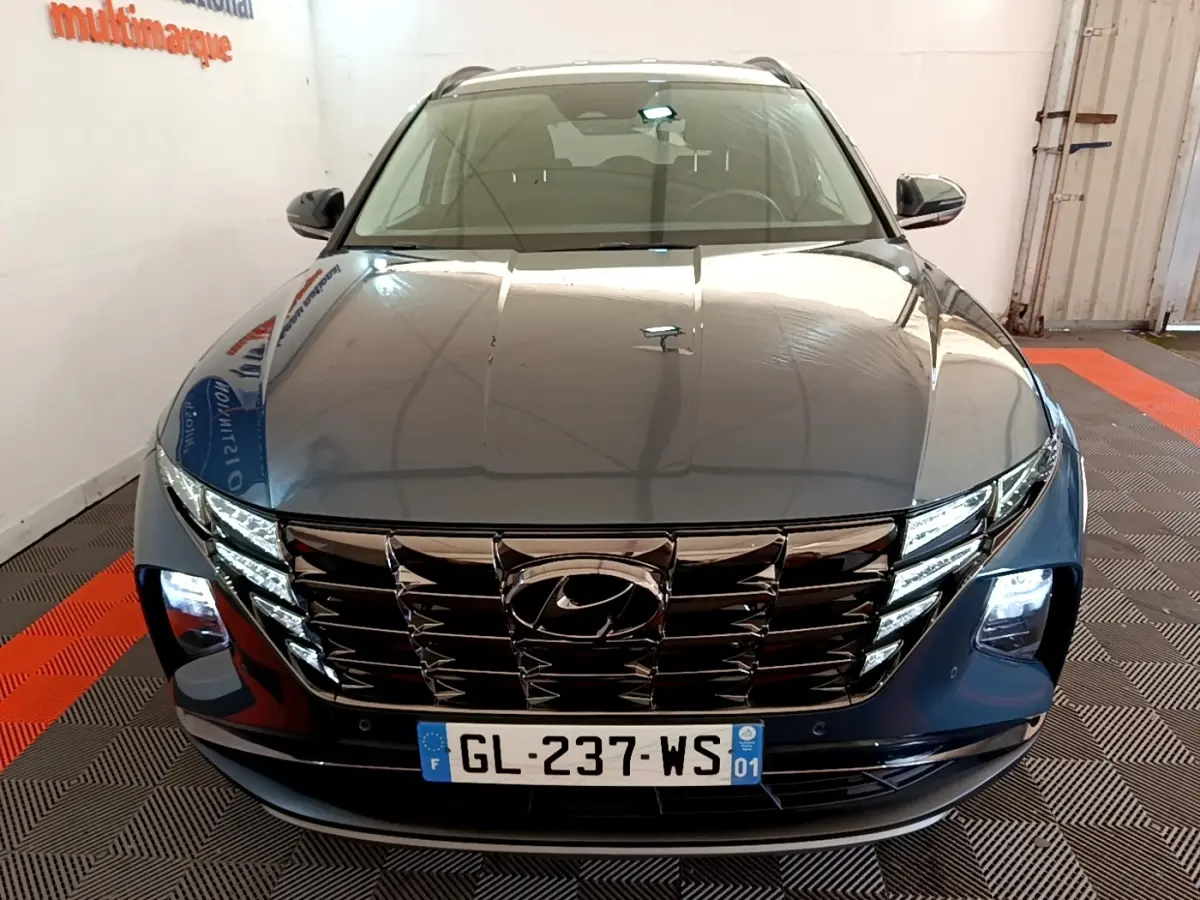 Vue avant d'un Hyundai Tucson bleu 2023 avec calandre chromée et phares LED allumés dans un showroom.