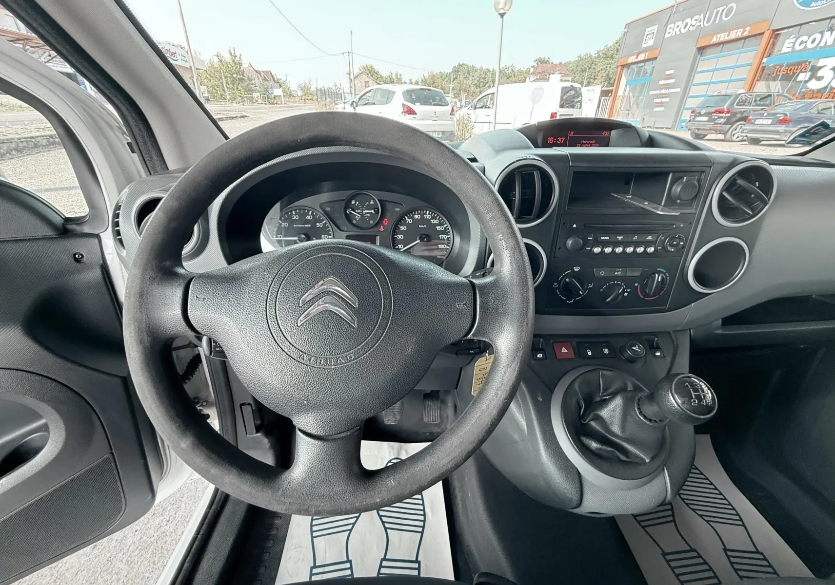 Vue intérieure du tableau de bord et volant noir du Citroën Berlingo blanc, avec levier de vitesses manuel visible.