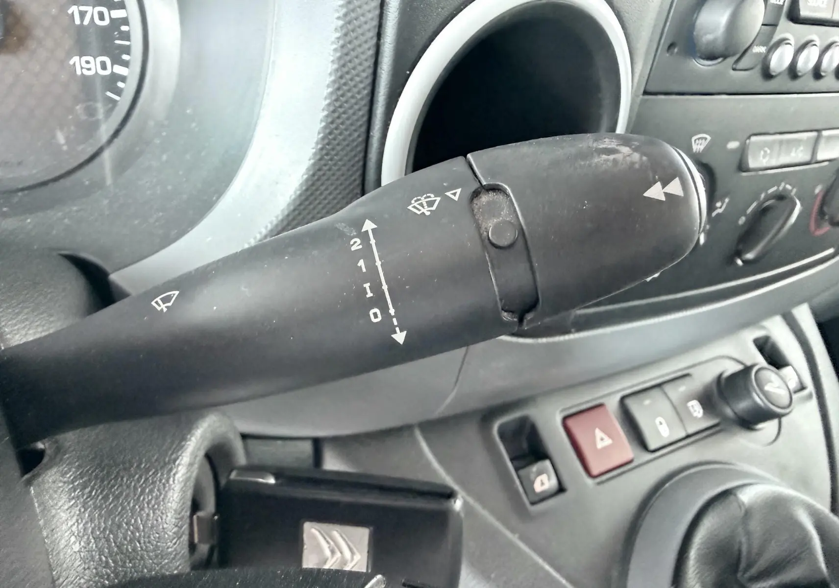 Gros plan sur la manette de commande des essuie-glaces du tableau de bord gris d’un Citroën Berlingo blanc de 2016.