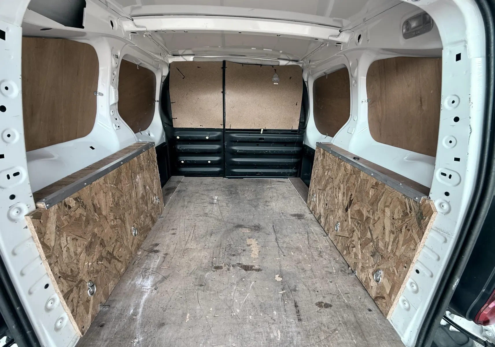 Vue intérieure arrière du Citroën Berlingo blanc 2016, montrant l’espace de chargement avec plancher et panneaux en bois.