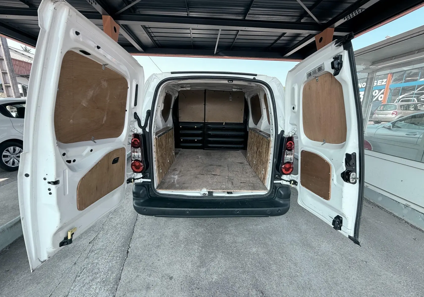 Vue arrière ouverte du Citroën Berlingo blanc 2016 montrant l'espace de chargement avec panneaux en bois.