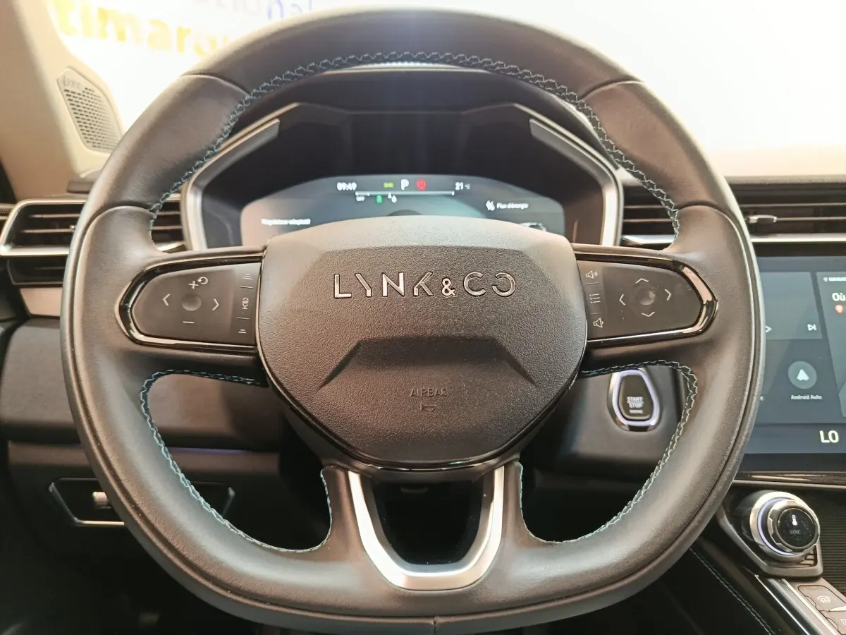 Vue rapprochée du volant noir du Lynk & Co 01 avec commandes tactiles et tableau de bord numérique en arrière-plan.