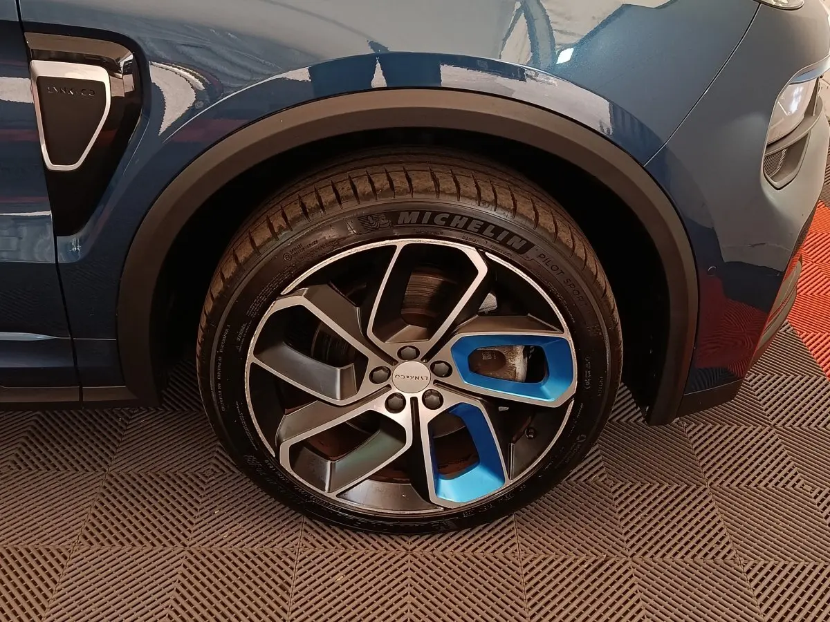 Gros plan sur la roue avant gauche bleu métallisé du Lynk & Co 01 avec jante alliage bicolore et logo central.