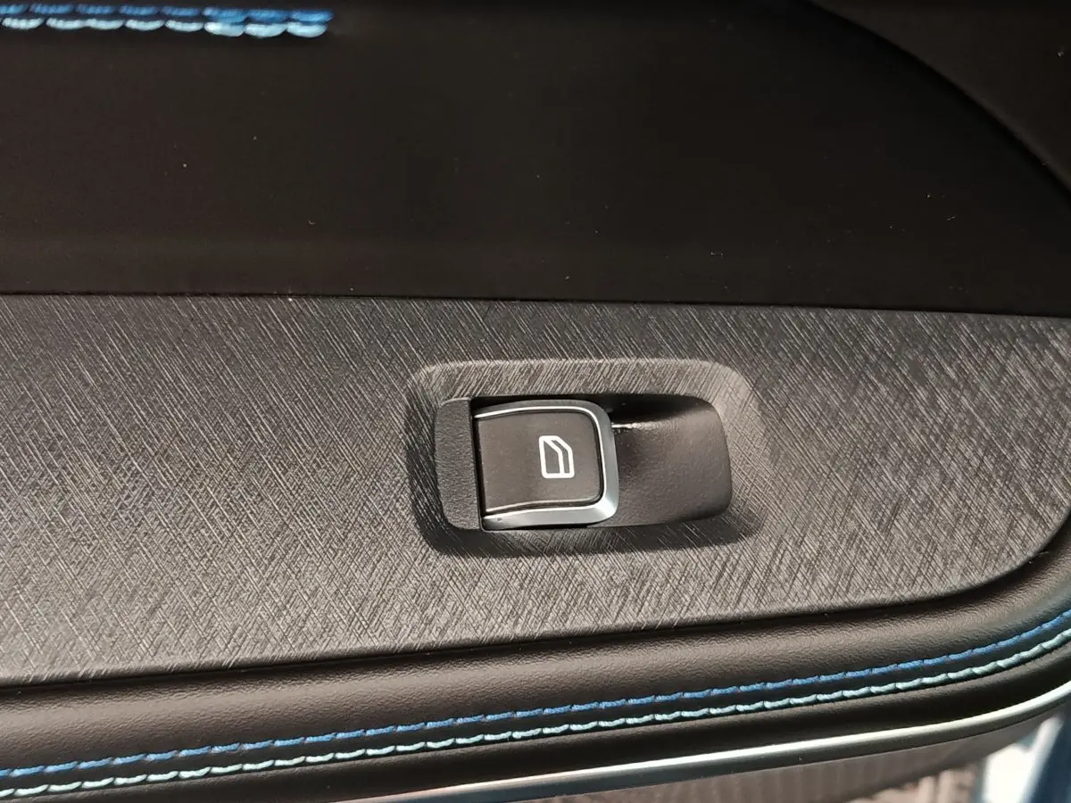 Gros plan sur le bouton de commande de vitre électrique sur la porte intérieure avec surpiqûres bleues du LINK & CO 01 hybride.