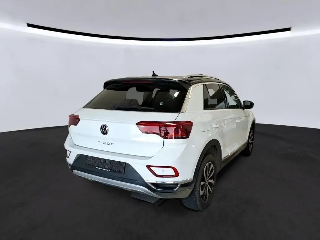 Volkswagen T-Roc blanc pur avec toit noir, vue 3/4 arrière droit, mettant en valeur ses feux arrière et jantes 17 pouces.