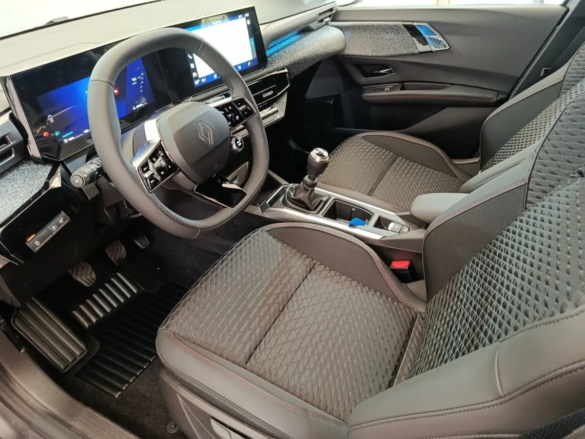 Vue intérieure côté conducteur de la Renault Clio techno TCe 115 essence 2026, avec sièges gris texturés et écran tactile large.