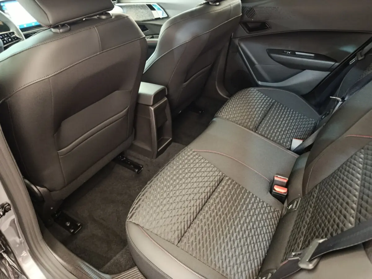 Vue intérieure arrière côté droit de la Renault Clio gris foncé, montrant la banquette avec surpiqûres rouges et l'accoudoir central.