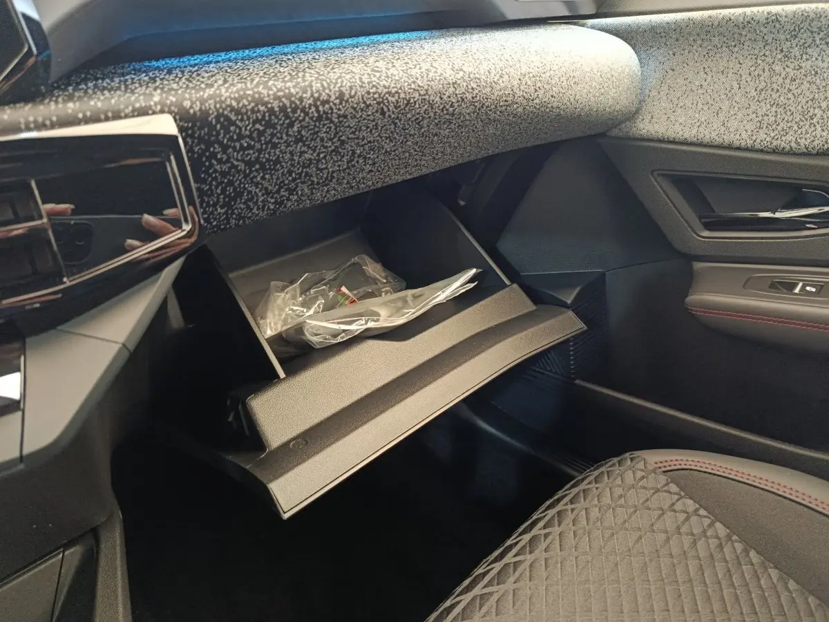 Intérieur de la Renault Clio Techno 2026, vue côté passager avec boîte à gants ouverte et sellerie noire à surpiqûres rouges.