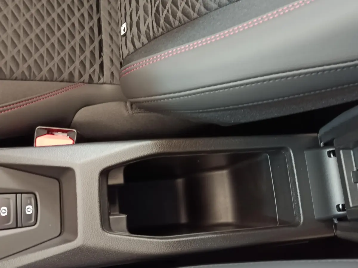 Gros plan sur l'accoudoir central avant ouvert de la Renault Clio Techno gris foncé avec surpiqûres rouges et sellerie tissu.