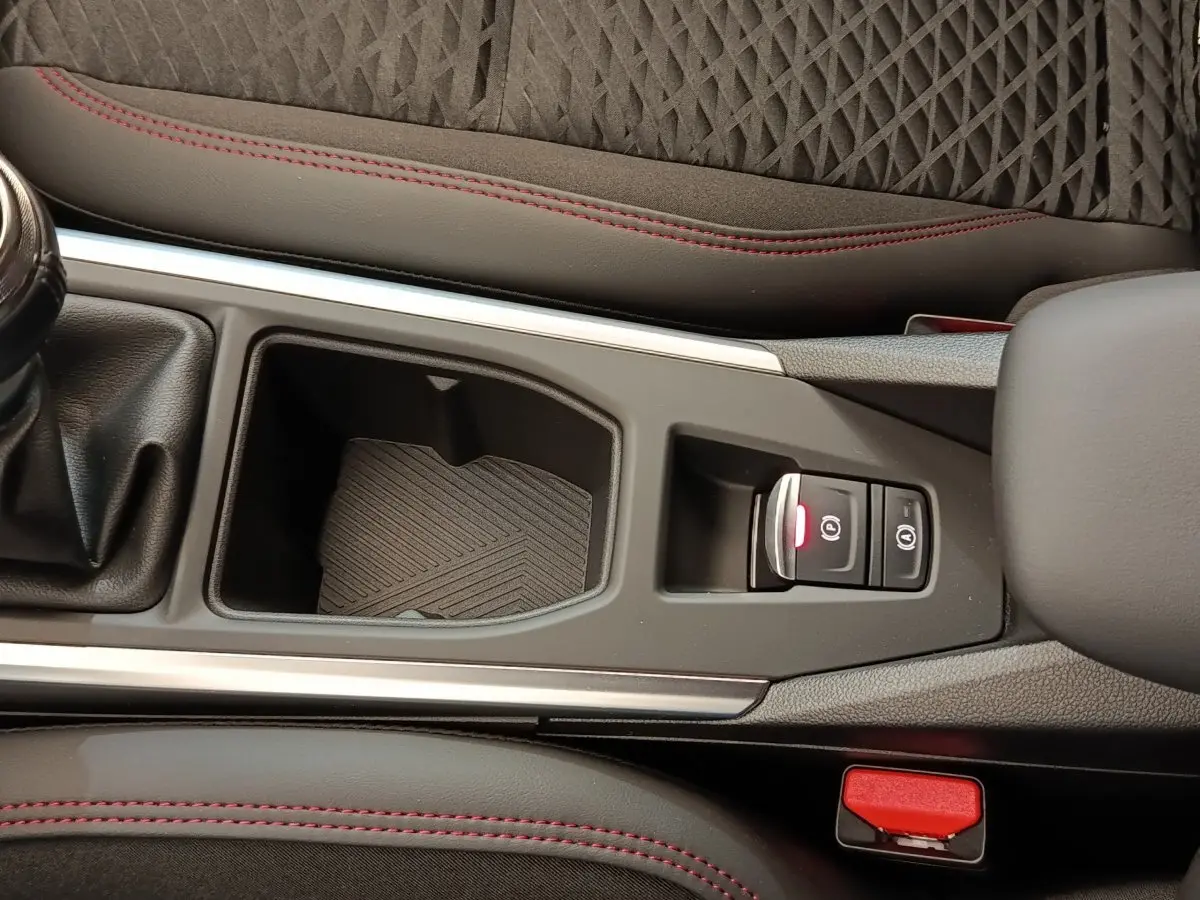 Vue rapprochée de la console centrale de la Renault Clio Techno gris foncé, avec frein à main électrique et surpiqûres rouges.