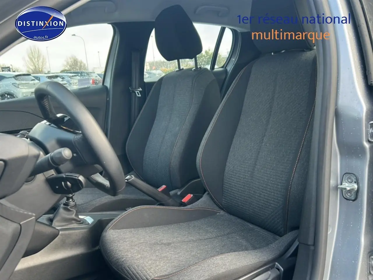 Vue intérieure côté conducteur de la Peugeot 208 1.2 100 style 2025 en gris artense, montrant les sièges et la boîte manuelle.