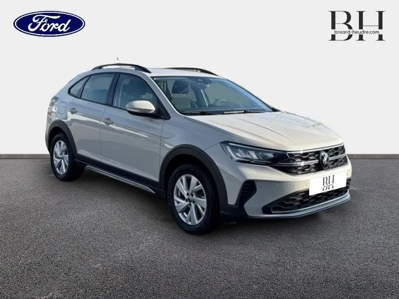 Volkswagen Taigo blanc pur en 3/4 avant droit, avec jantes alu et barres de toit visibles.