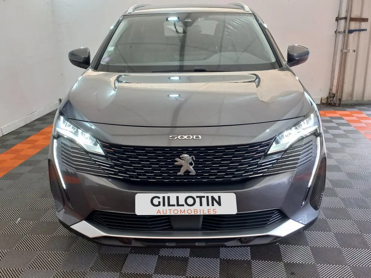 Vue avant d’un Peugeot 5008 gris foncé avec calandre noire et phares LED allumés dans un garage.