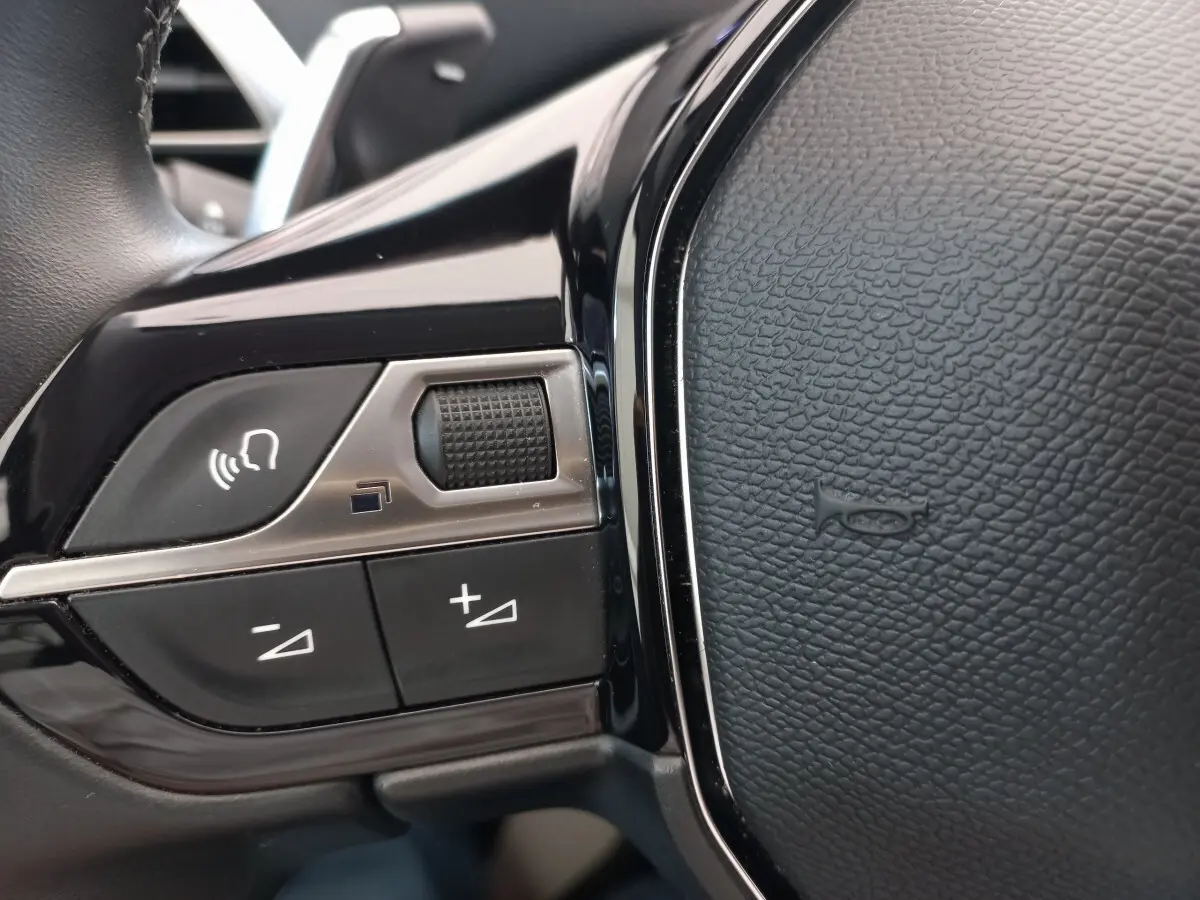 Gros plan sur les commandes vocales et volume du volant cuir noir du Peugeot 5008 gris foncé, version 2021.