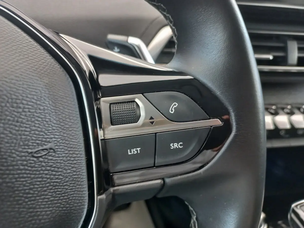 Gros plan sur les commandes gauche du volant cuir noir du Peugeot 5008 gris foncé, avec boutons LIST et SRC visibles.