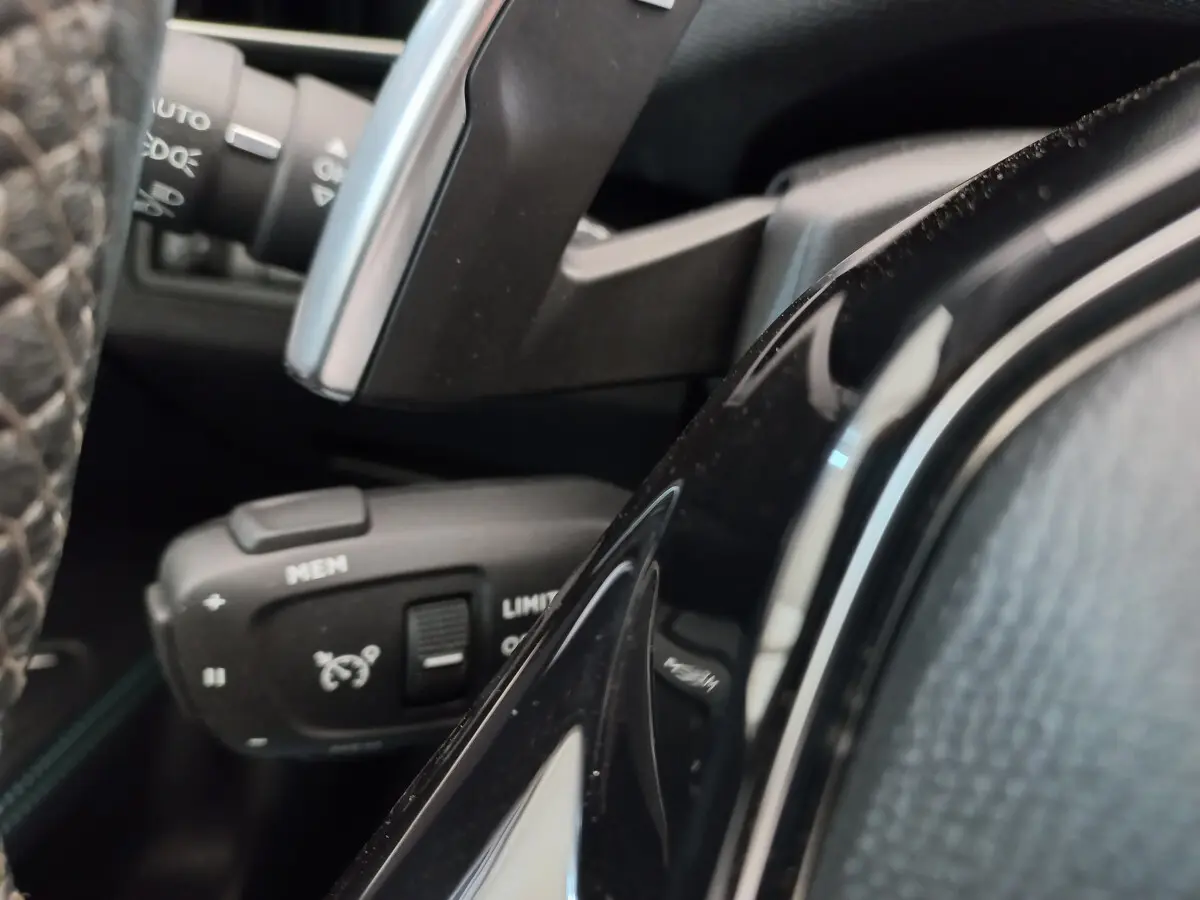 Gros plan sur la commande de régulateur de vitesse à gauche du volant du Peugeot 5008 gris foncé, intérieur noir.
