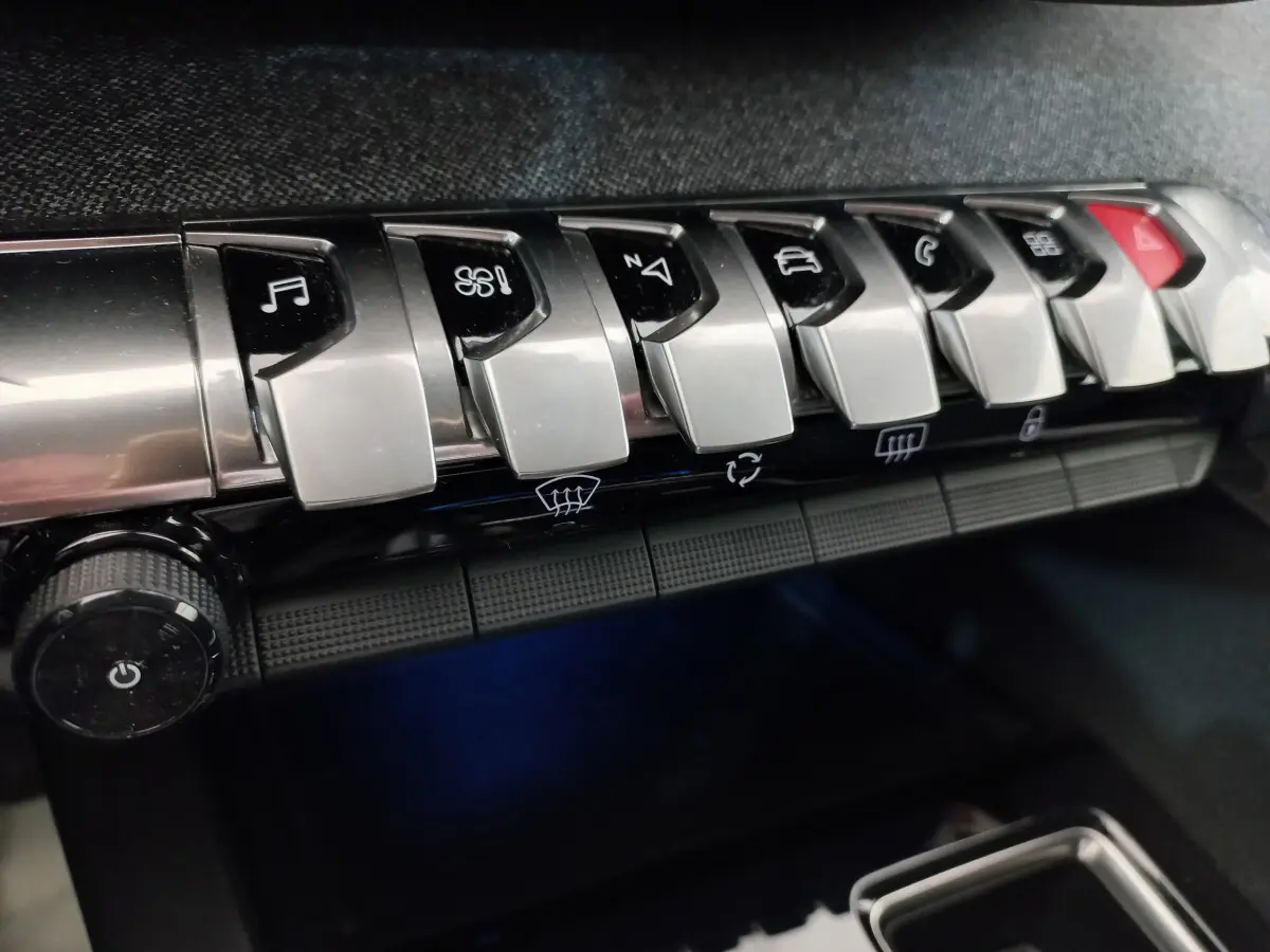 Gros plan sur les commandes chromées du tableau de bord du Peugeot 5008 gris foncé, avec boutons multifonctions et climatisation.