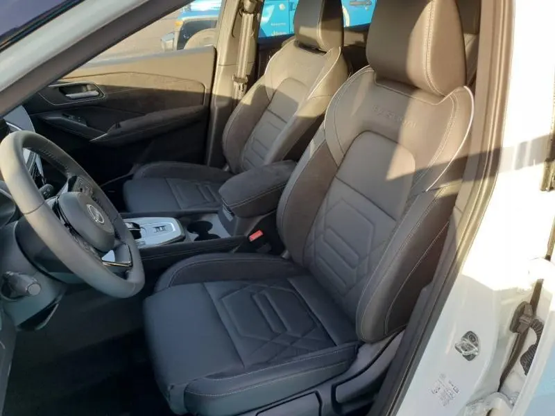 Vue intérieure côté gauche montrant les sièges avant noirs en tissu et cuir avec surpiqûres et logo Nissan embossé.