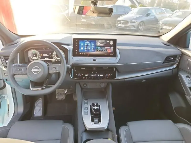 Vue intérieure avant du Nissan Qashqai Hybrid e-POWER 2025, tableau de bord moderne avec écran tactile et volant multifonction.