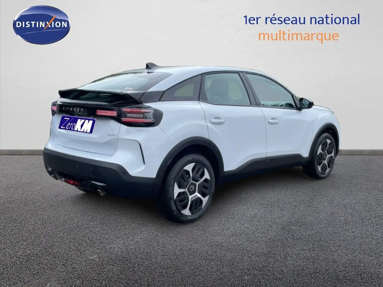 Vue 3/4 arrière droite d'une Citroën C4 blanche métal avec toit noir et jantes distinctives, stationnée sur sol gris.