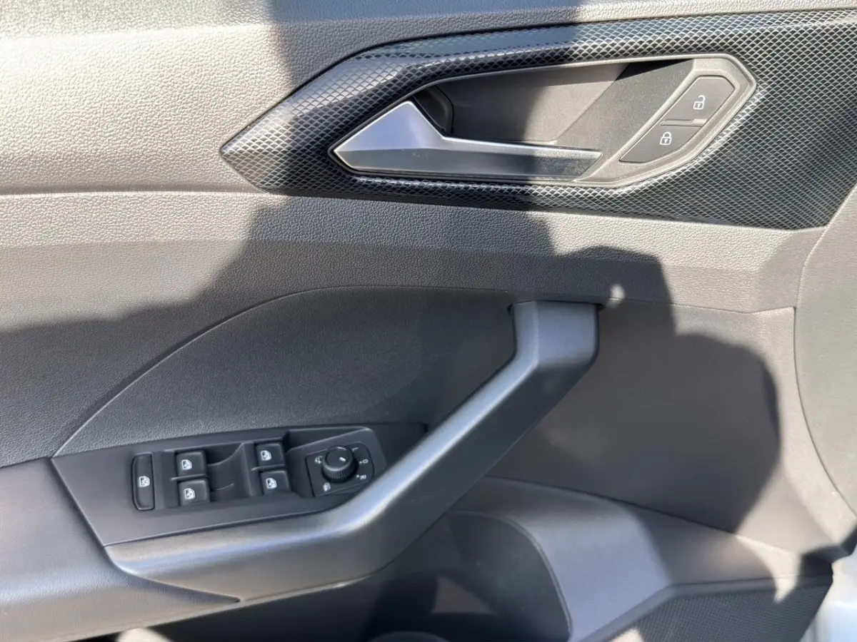 Gros plan sur la porte côté conducteur du Volkswagen T-Cross gris clair, montrant les commandes de vitres et de verrouillage.