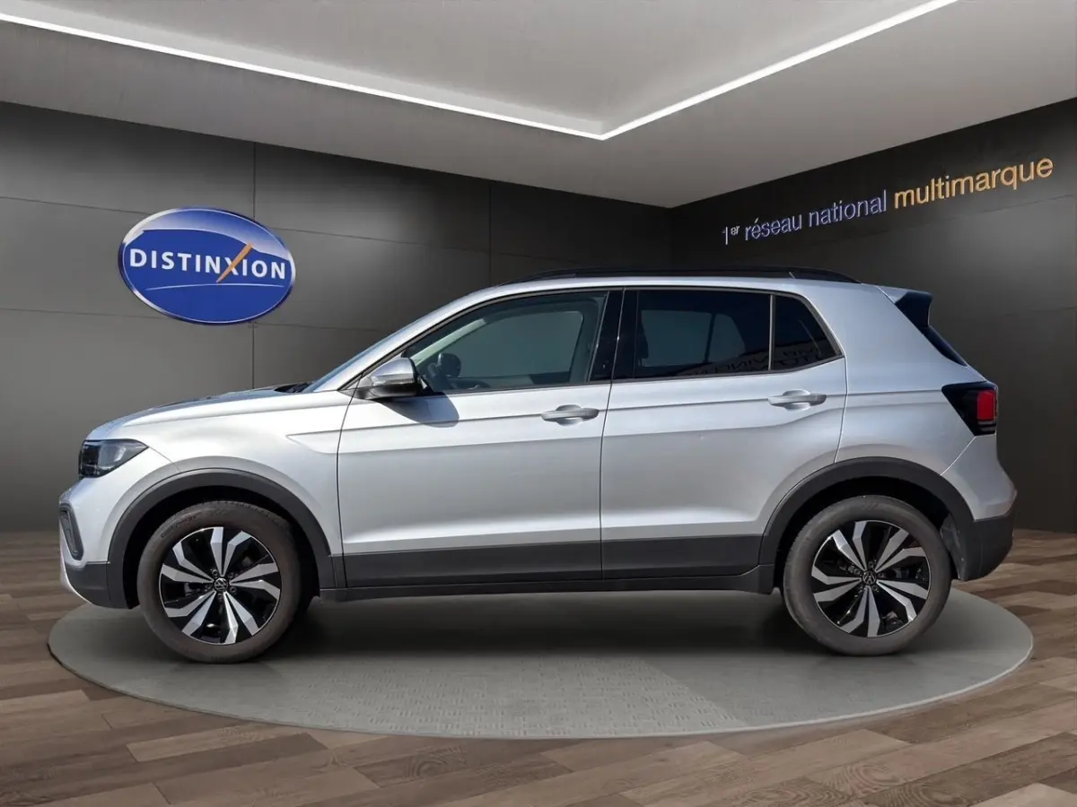 Vue de profil côté gauche d'un Volkswagen T-Cross gris clair avec jantes alliage et barres de toit noires.