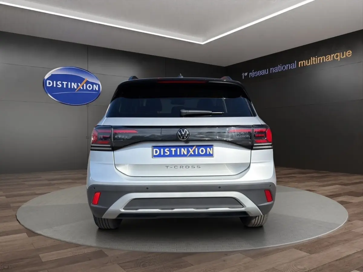 Vue arrière d'un Volkswagen T-Cross gris clair avec feux LED et logo VW visible sur fond showroom.