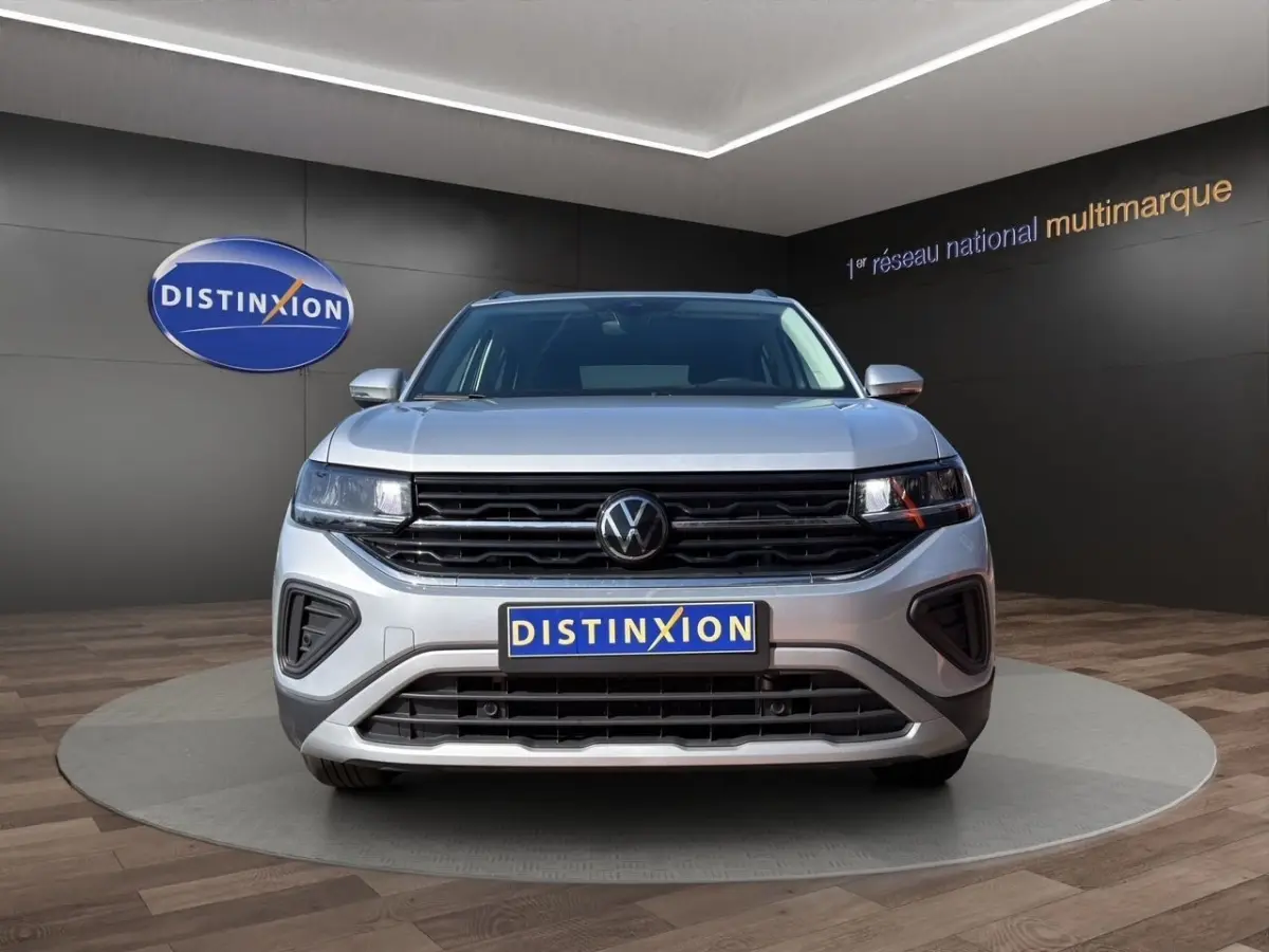 Vue de face du Volkswagen T-Cross gris clair 2025 avec calandre noire et logo VW centré, en showroom.